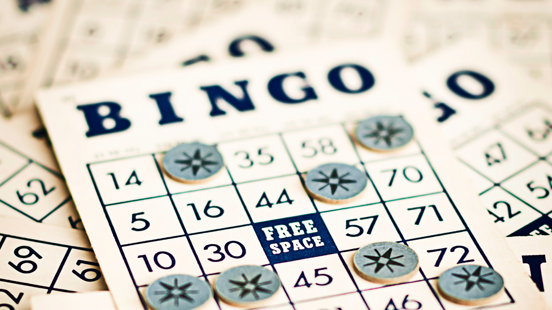 Pile of bingo cards, the topmost with bingo markers on some squares.