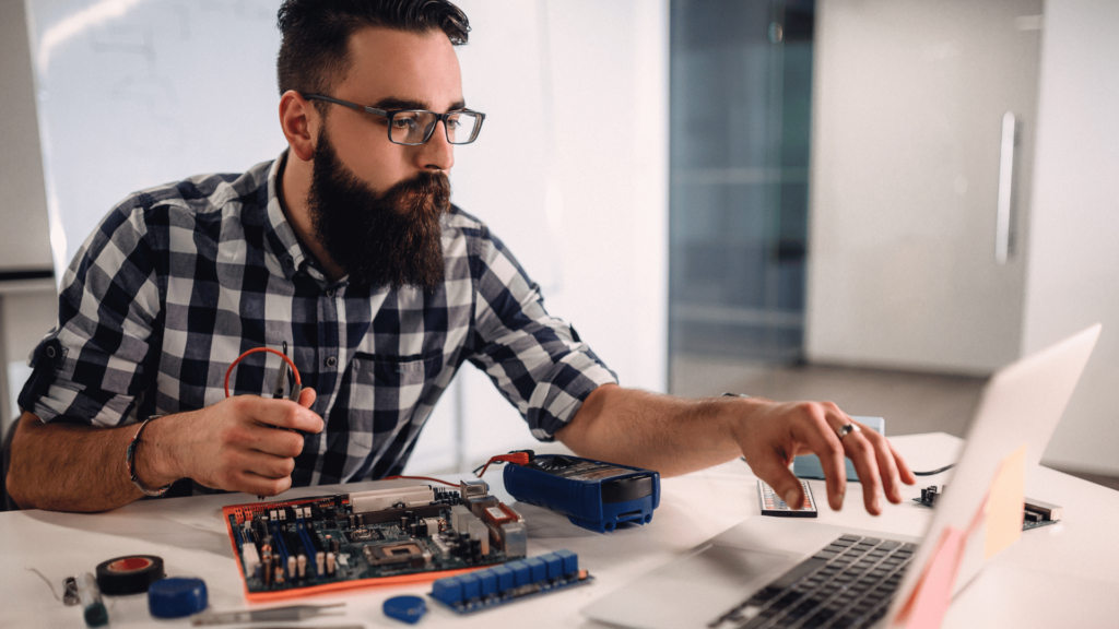 Man working on laptop with computer technology on the desk in front of him.