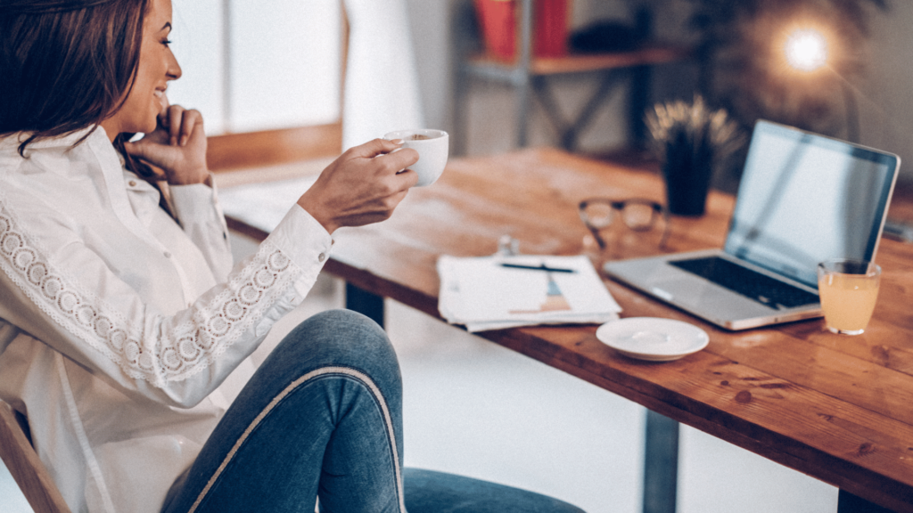 Woman sits comfortably at her desk in her home office, happy with a coffee mug.