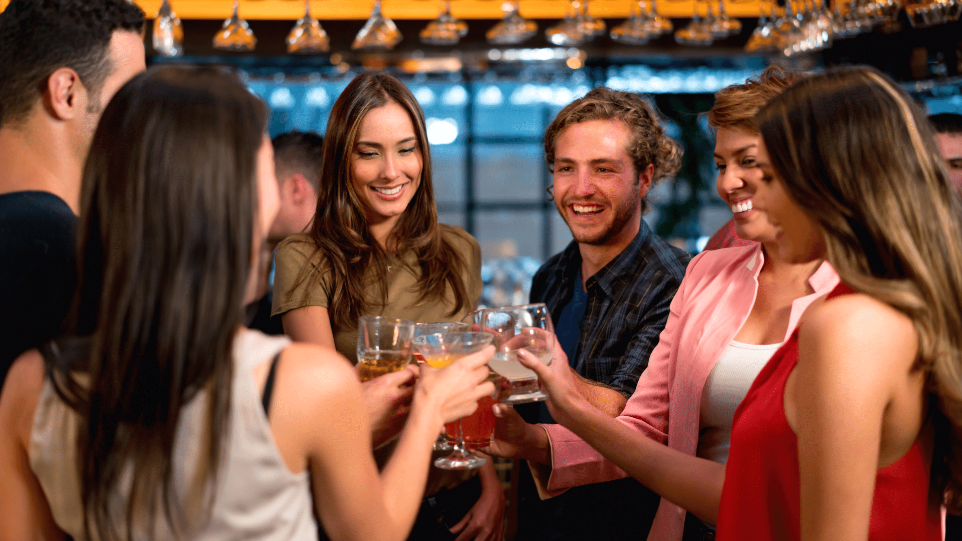 Group of young adults at an evening event, tapping their cocktails together in 'Cheers'