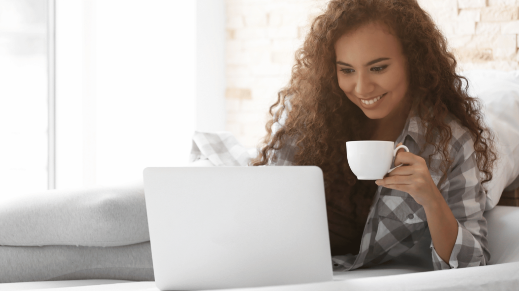 Woman holding tea cup, smiling at her laptop screen.